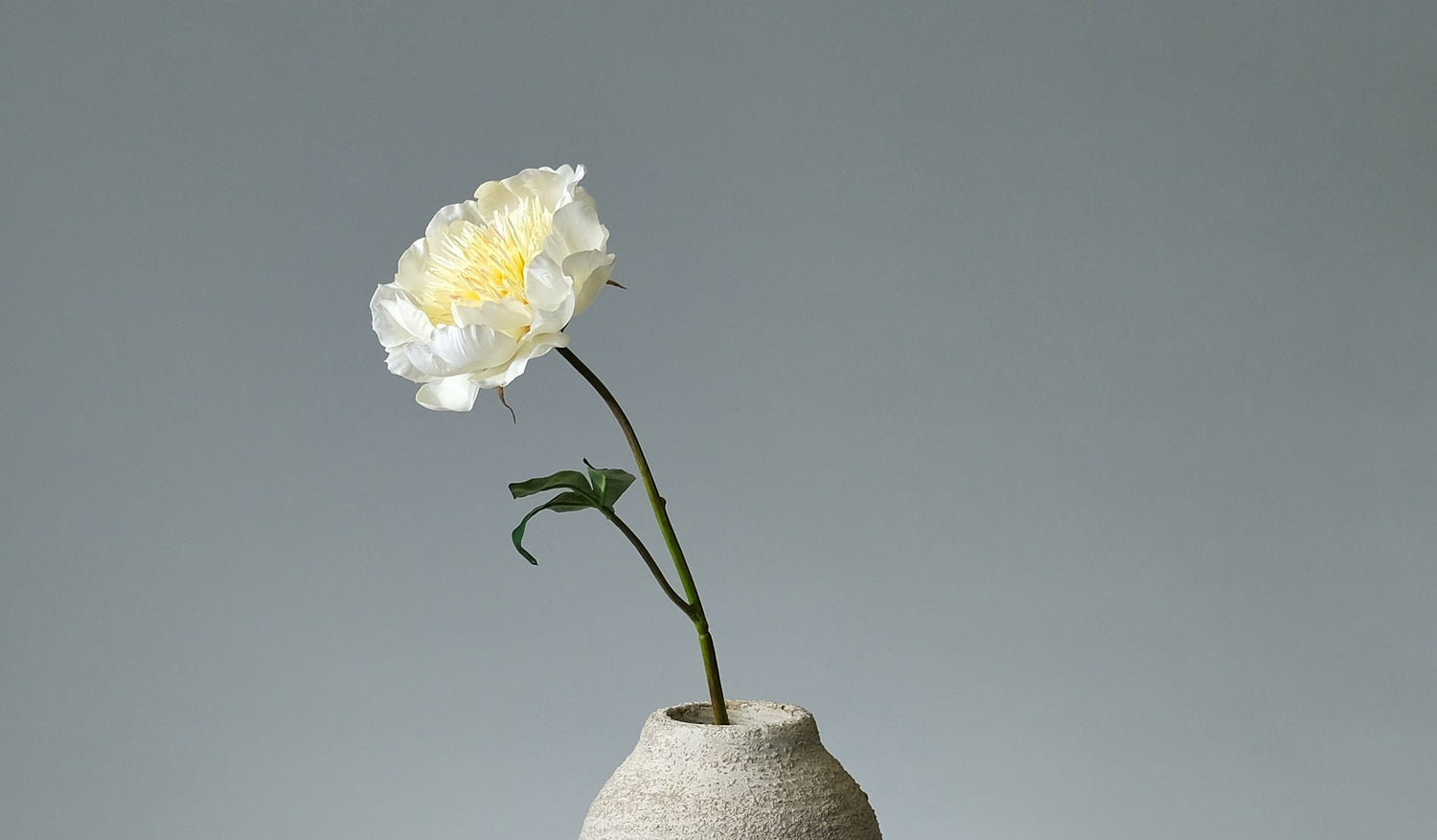 Olika konstgjorda snittblommor i naturliga färger, arrangerade tillsammans – inklusive rosor, ranunkler, pioner och gröna blad i en ljus och stilren miljö. Florissma
